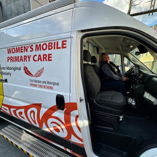 A woman smiles in the driver's seat and the van reads Women's Mobile Primary Care
